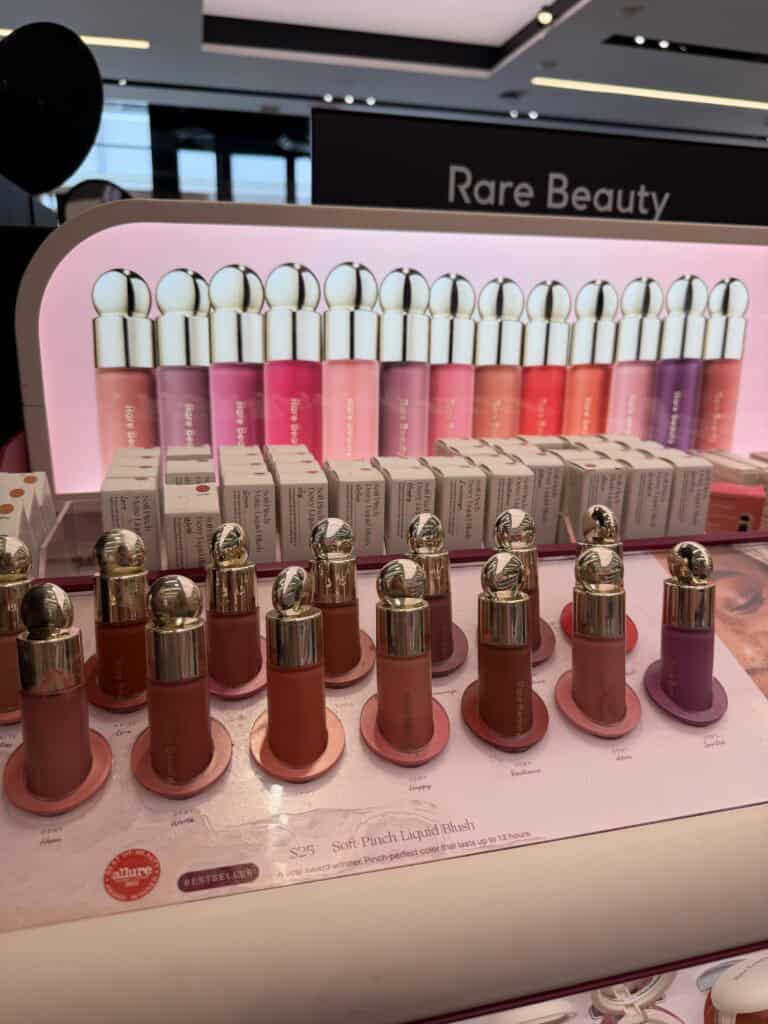 Rare Beauty Soft Pinch Liquid Blush display at Sephora showing the full shade range including Hope, Worth, Happy, Resilience, Adore, and Spirited on a pink-lit countertop