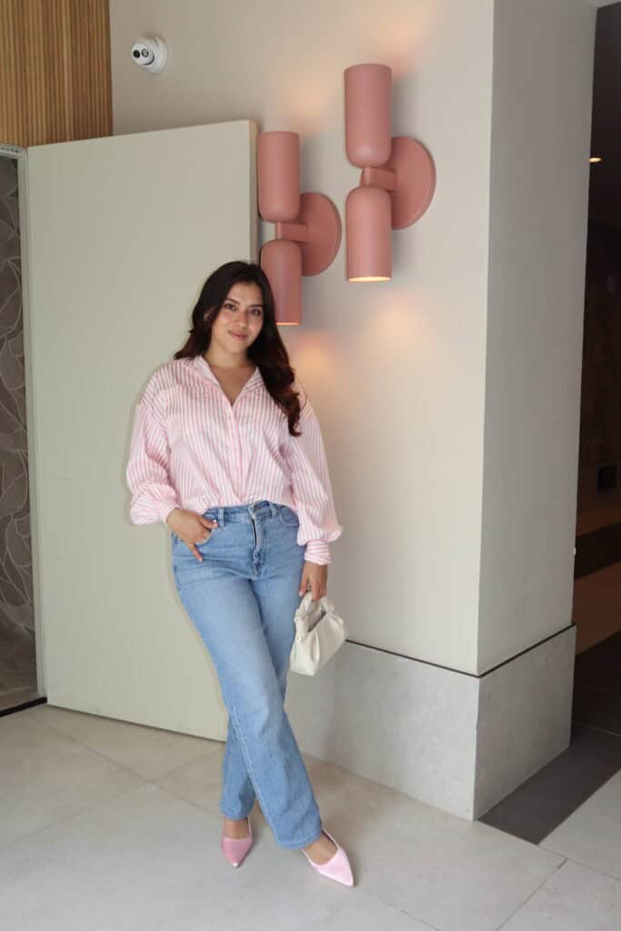 Jasmine Del Toro wearing high-rise straight leg light wash jeans with an oversized pink striped button-down shirt and pink pointed-toe heels – a real outfit example of the best types of jeans for a petite curvy hourglass figure