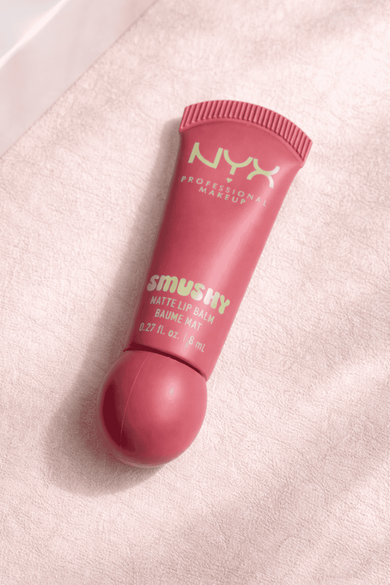 NYX Professional Makeup Smushy Matte Lip Balm tube in Snuggle SZN lying on a soft pink textured surface