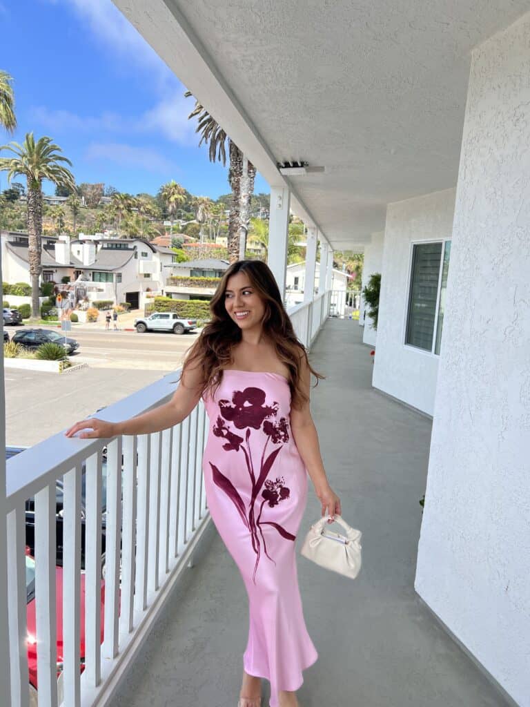 Jasmine Del Toro wearing a pink floral satin midi dress and white mini bag – a spring wedding guest dress idea in Southern California