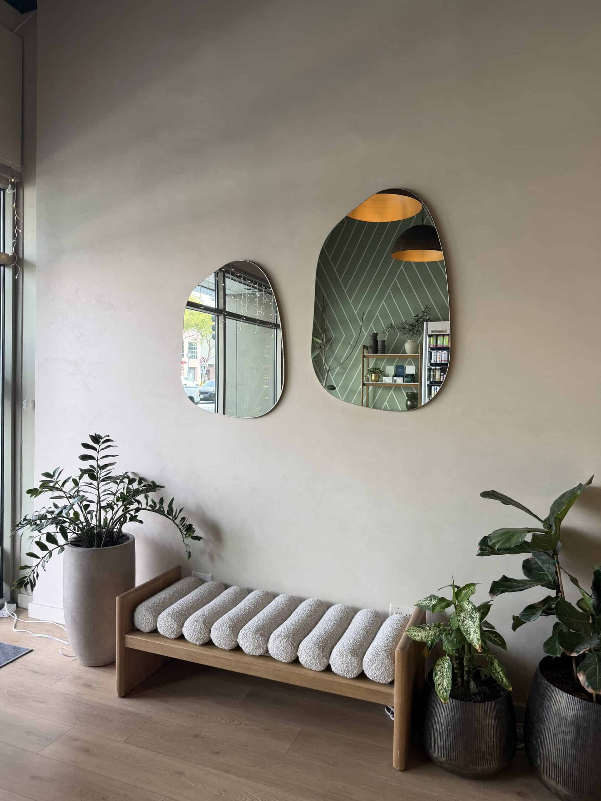A serene minimalist interior in Los Angeles with two organic-shaped mirrors, a white boucle bench, and lush green houseplants – the kind of calm, intentional space that inspires you to slow down and explore passion project ideas that are good for your soul- Layers of Beauty